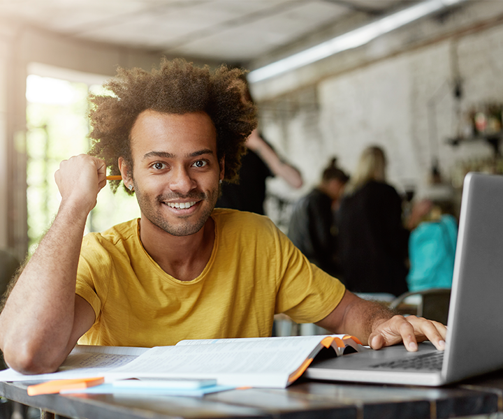 feliz positivo afroamericano estudiante universitario con alegre linda sonrisa usando conexión inalámbrica a internet en la computadora portátil