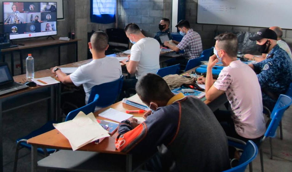 hombres en aula de clase observando videoconferencia en computador.