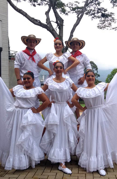 Cinco de integrantes de grupo de danza posan para la fondo con sus vestidos tradicionales de baile