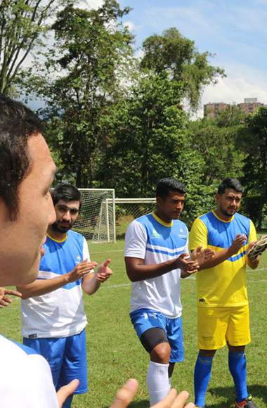 Cuatro universitarios reunidos en una cancha de futbol mientras escuchan la charla técnica. 