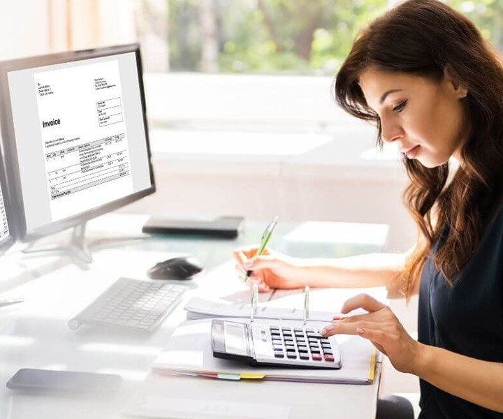 Los nuevos desafíos del contador Mujer frente a dos pantallas de computador,las cuales contienen datos, números y estadísticas. Ella se encuentra escribiendo mientras realiza cuentas en una calculadora