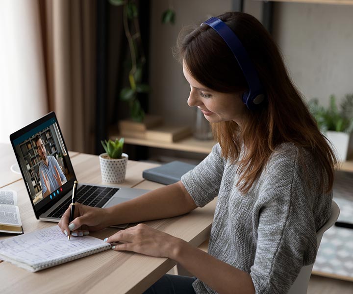 Persona usando audífonos  tomando nota en una reunión virtual.