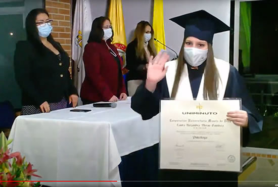 Graduada UNIMINUTO recibe su diploma con toga, birrete y tapabocas. 
