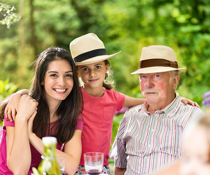 Tres personas reunidas en una foto familiar donde está un señor mayor, una mujer y una niña. Un fondo con naturaleza de color verde