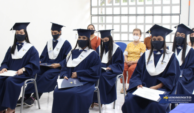 Estudiantes sentados  con toga en la ceremonia con su diploma