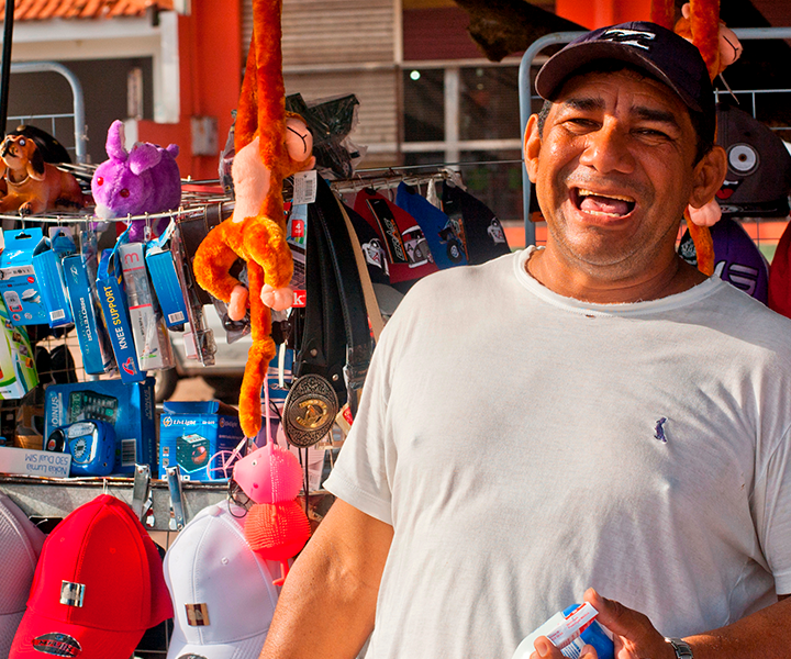 Vendedor informal sonriendo, al fondo se ve su puesto de trabajo con los productos.