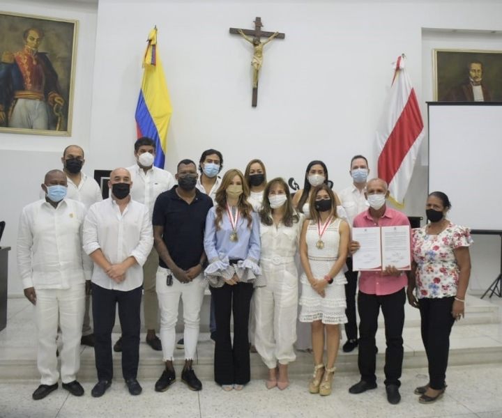 Cuatro mujeres vestidas de blanco una tiene una medalla y pergamino de reconocimiento