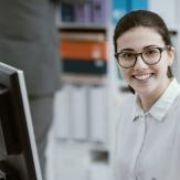 persona sonriente frente a un computador y con estanterías de archivos detrás