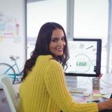 Mujer sentada frente a un computador, voltea sonriente para mirar a la cámara