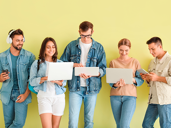 Estudiantes con dispositivos modernos cerca de la pared de color verde, buscando Proyectos sociales de formación