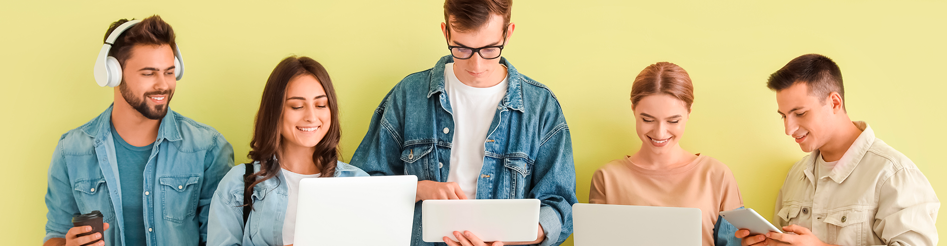 Estudiantes con dispositivos modernos cerca de la pared de color verde, buscando Proyectos sociales de formación