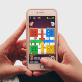 Manos sosteniendo un celular, en la pantalla se ve la app del juego Parchís. 