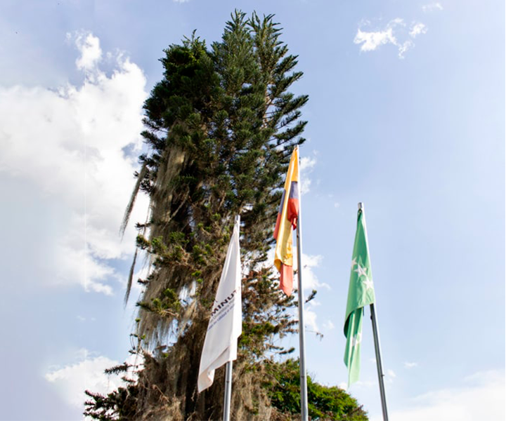 Banderas de uniminuto, colombia y risaralda, con paisaje de fondo 