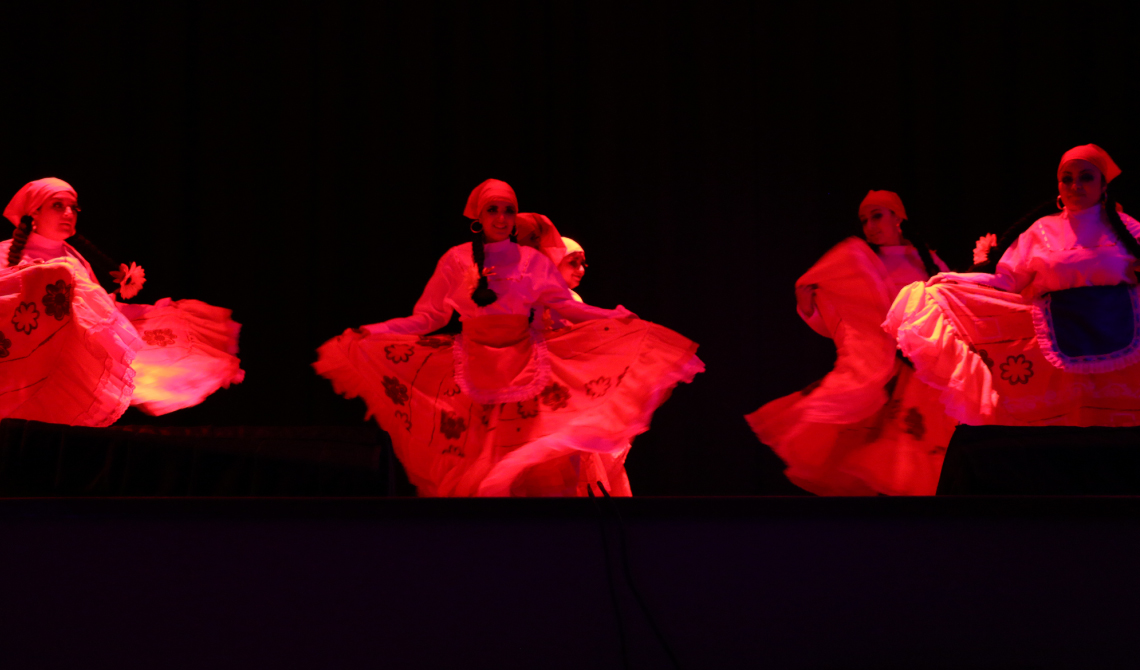 Mujeres bailando con falda larga, trenzas y pañoleta sobre la cabeza. 