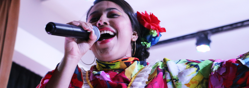Mujer usando traje típico, cantando con un micrófono de mano.