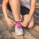 Una persona arrodillada amarrando sus tenis, preparándose para realizar deporte. 