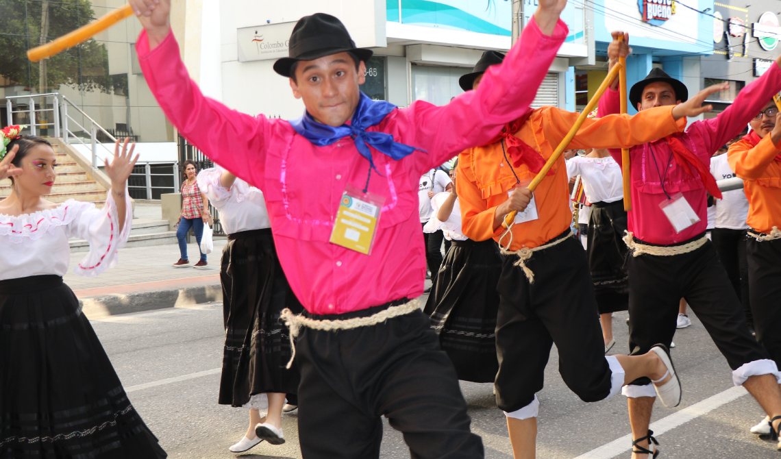 Grupo de hombres danzando con coloridas camisas, sombreros negros, pañoletas y bastones.