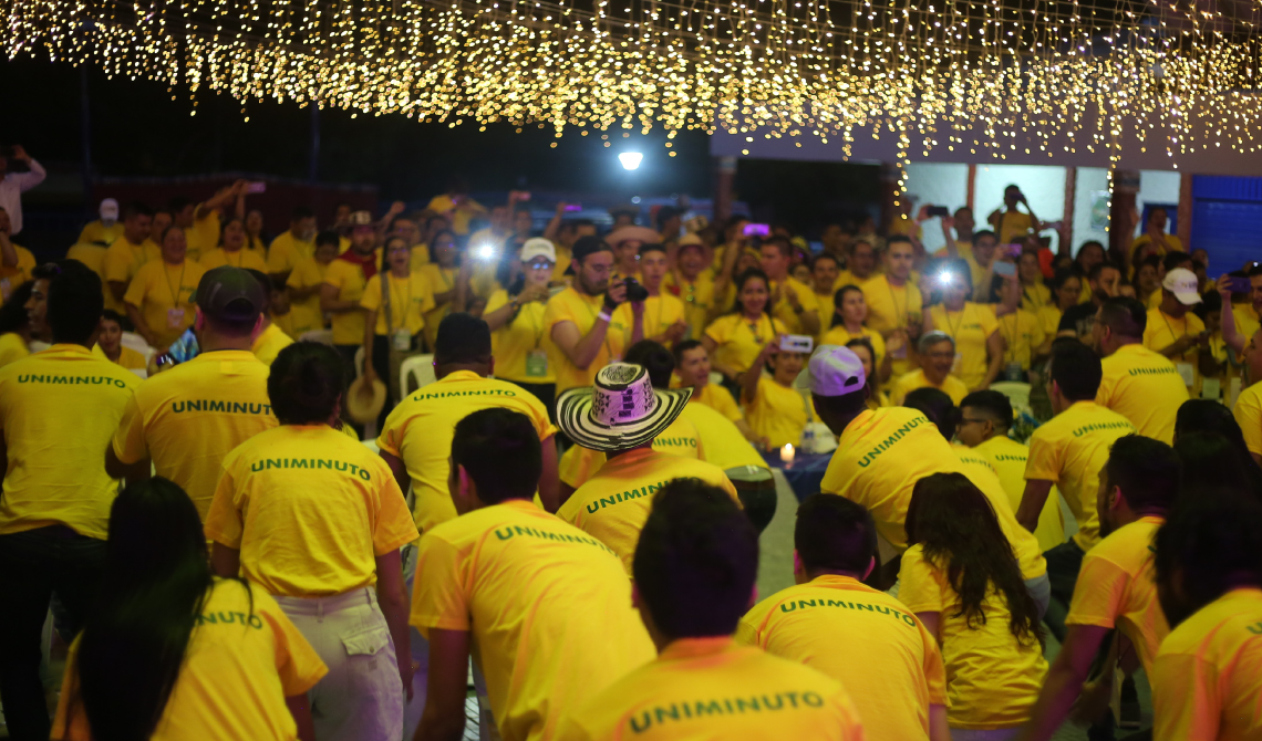 Estudiantes con camisetas amarillas bailando alegres bajo lucecitas colgantes.