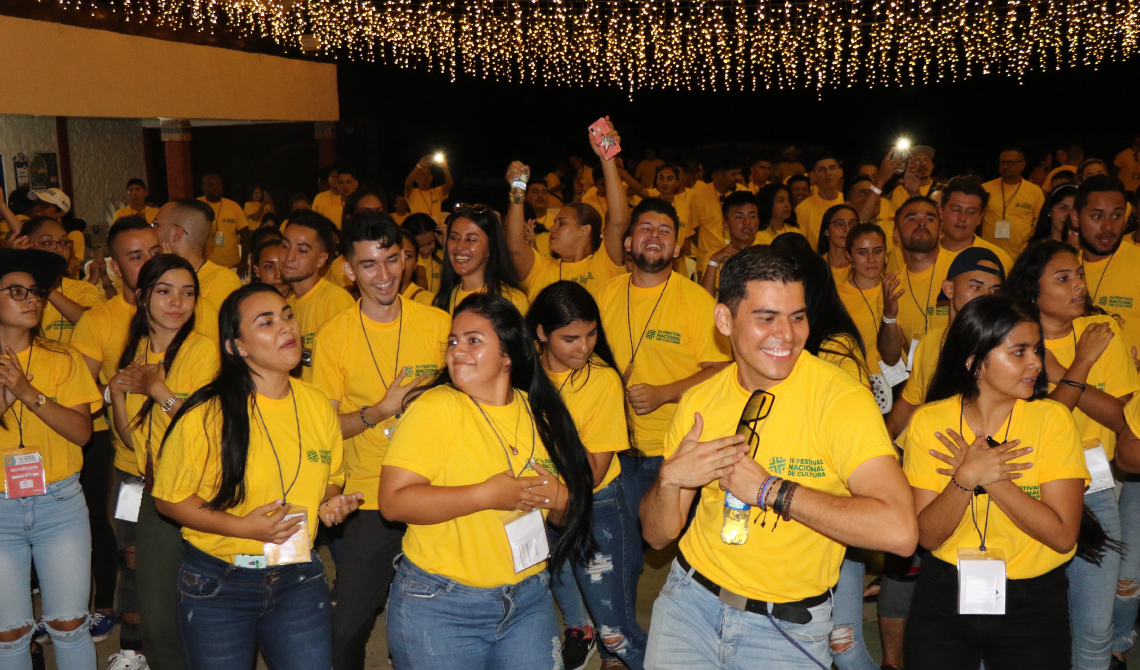 Estudiantes con camisetas amarillas bailando alegres bajo lucecitas colgantes.