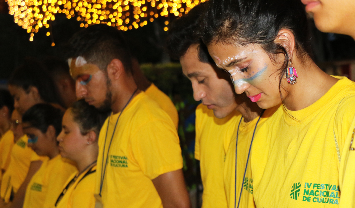 Primer plano de estudiantes con los ojos cerrados, escuchando la oración de bienvenida. 