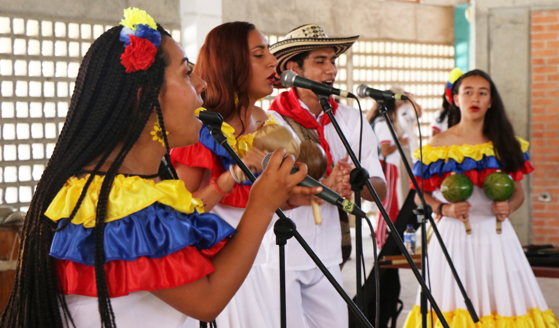 Grupo con trajes de colores de la bandera, cantando y agitando maracas.