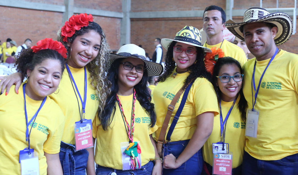 Grupo de estudiantes con camisetas amarillas, sombreros y flores rojas en el cabello, posando para la cámara.