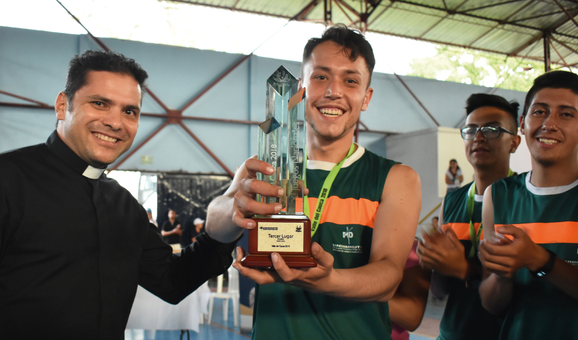 Jugador de equipo de fútbol, recibiendo sonriente el trofeo de tercer lugar.