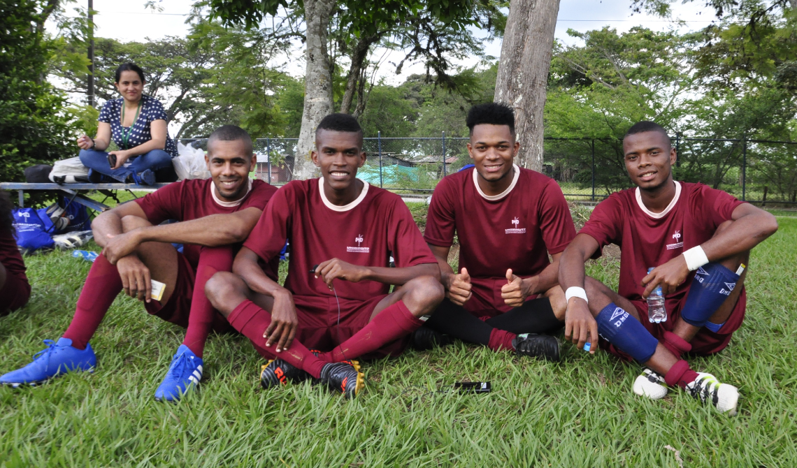 Estudiantes del equipo de fútbol masculino del Centro Regional Urabá, sentados alegres en el césped.