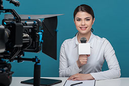 Mujer hablando por micrófono frente a una cámara sonriendo