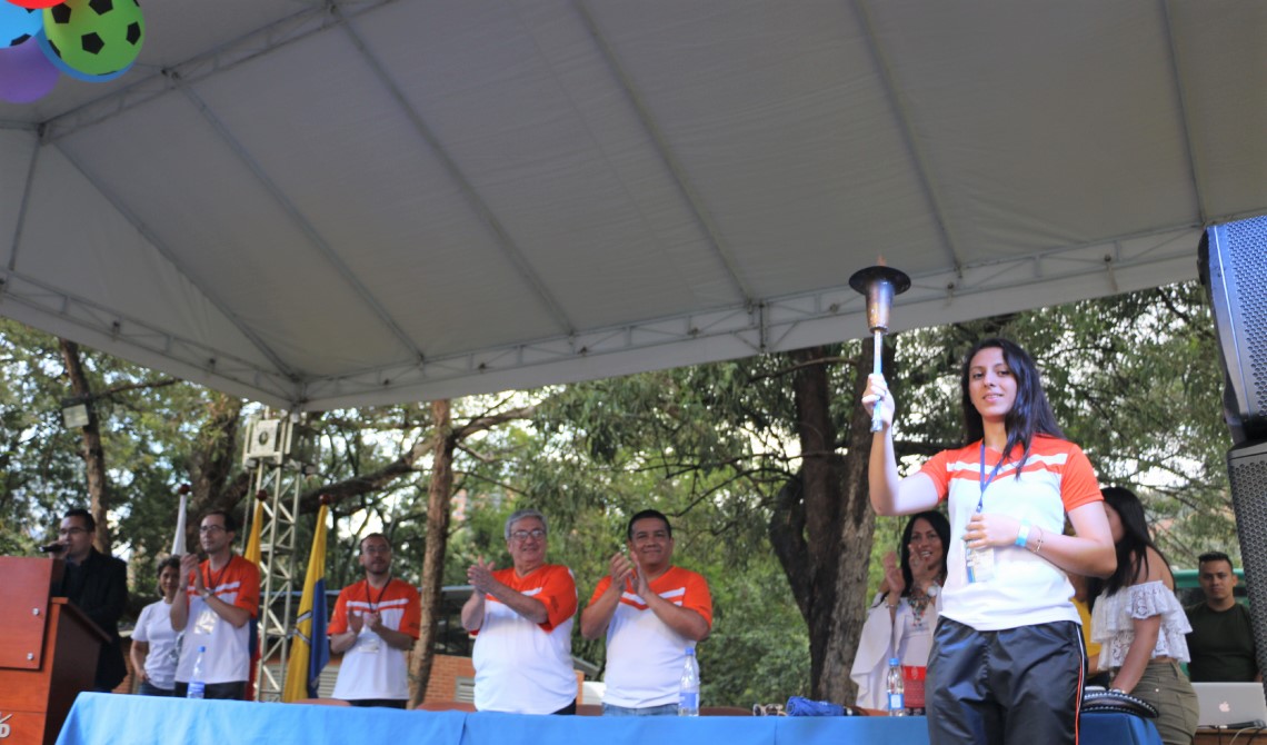 Estudiante sujetando la llama olímpica en tarima, junto a los directivos de la Institución.
