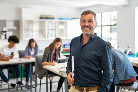 Hombre al frente sonriendo con salón de clases de fondo