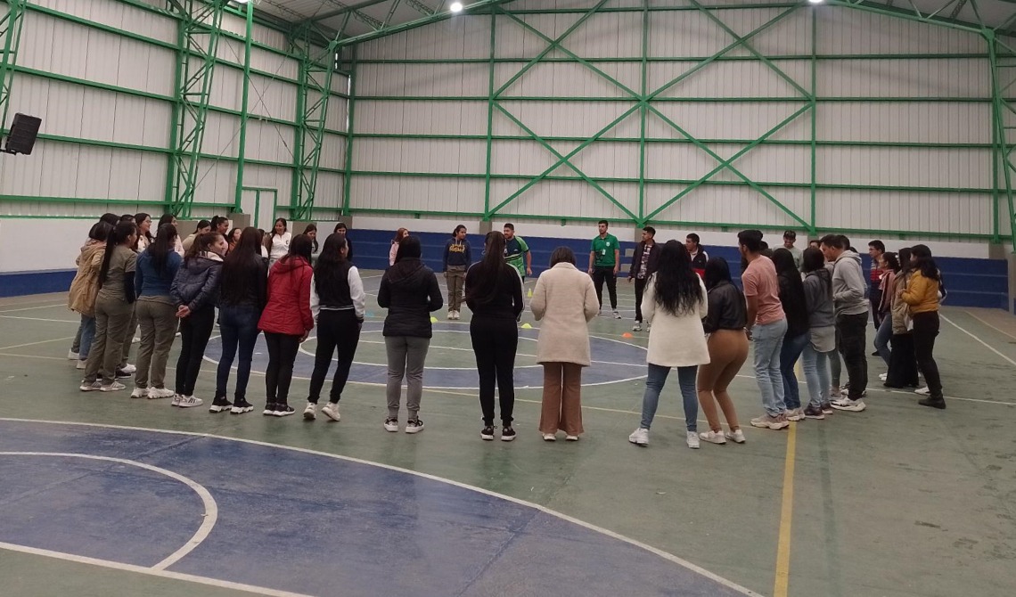 Grupo de personas en círculo realizando una actividad en un coliseo.