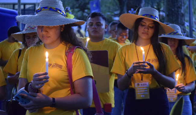 Estudiantes orando con una vela prendida en sus manos