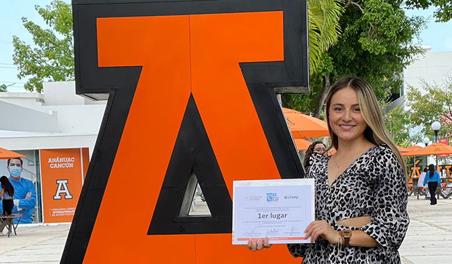 Estudiante ganadora del concurso junto al logo de la Universidad Anáhuac de Cancún de México.
