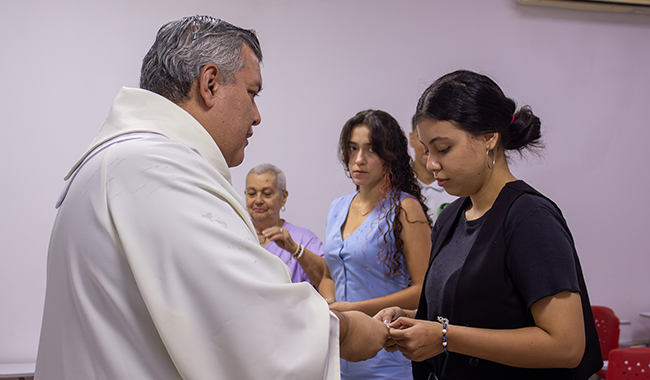 El capellán entrega el pin institucional Cruz Minuto de Dios a una estudiante de Trabajo Social durante la ceremonia de envío.