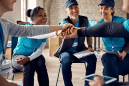 Grupo diverso de trabajadores sociales sentados en círculo durante una reunión, colocando sus manos juntas en el centro como gesto de trabajo en equipo y compromiso comunitario