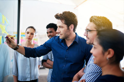 Grupo de personas colaborando y señalando información en una pantalla durante una reunión de trabajo.