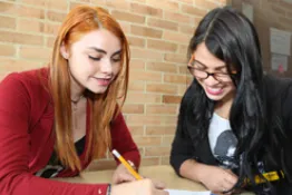 Dos estudiantes interactuando entre ellos mientras toman apuntes en una agenda