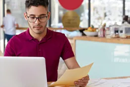Un hombre con una hoja en la mano en frente de un computador