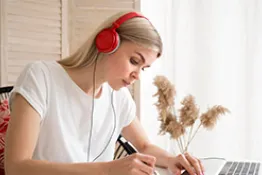 Mujer  con audífonos sentada en escritorio escribiendo 