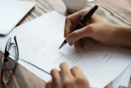 Primera plano de mesa donde se observan unas manos firmando un documento