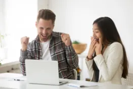 Joven pareja sentada en escritorio celebrando frente a un computador