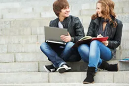 Pareja estudiantes con un computador, sentados en unas escaleras