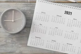 Reloj despertador junto con calendario y bolígrafo sobre escritorio