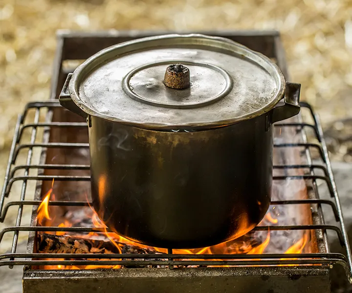 Olla de metal con tapa sobre una parrilla de hierro sobre un fuego generado por una estufa ecológica