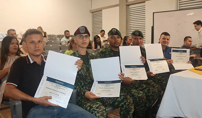 Grupo de participantes, incluidos miembros del Ejército Nacional, sostienen sus certificados durante la ceremonia del curso de drones en aula.
