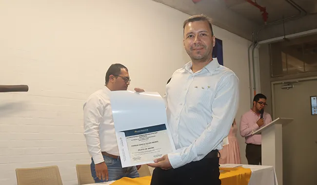 Hombre recibe su certificado durante la ceremonia de graduación del Curso Piloto de Dron en un auditorio.