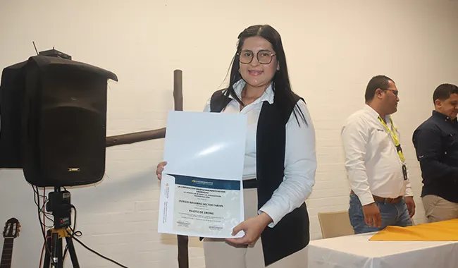 Mujer sostiene su certificado frente a una cámara durante la ceremonia de graduación del curso de drones.