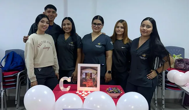 rupo de estudiantes posando junto a una decoración con globos blancos y rojos en forma de corazón.