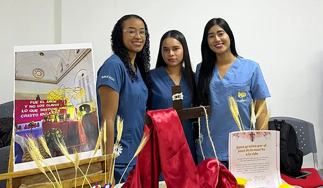 Tres estudiantes junto a una muestra decorativa con elementos religiosos y culturales.